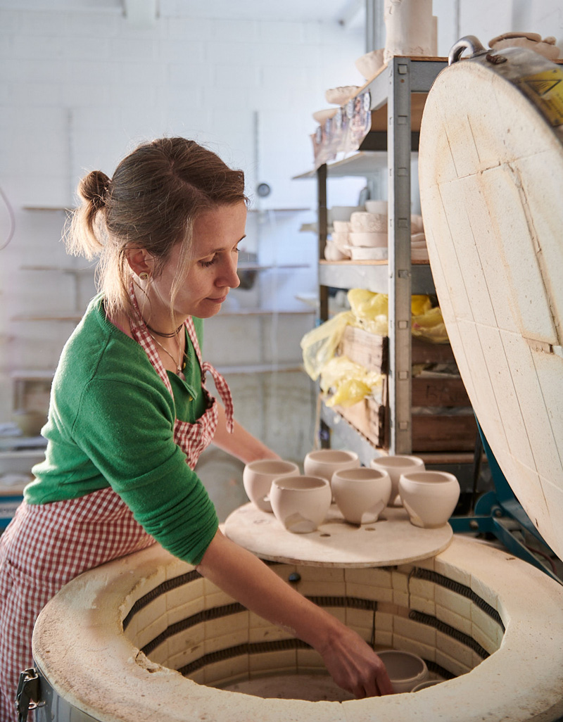 Handwerk_Ton-Studio_Brennofen Kerstin Habersack steht vor einem Brennofen, den sie mit getöpferten Tassen befüllt.