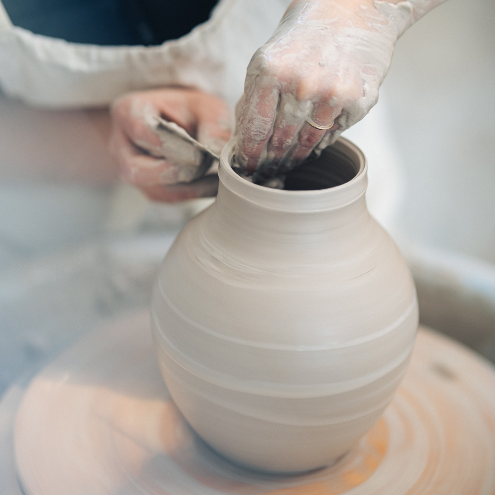 Keramikstudio | Tonstudio Kurs: Zwei Hände die an einer Töpferscheibe einen Krug aus Ton drehen