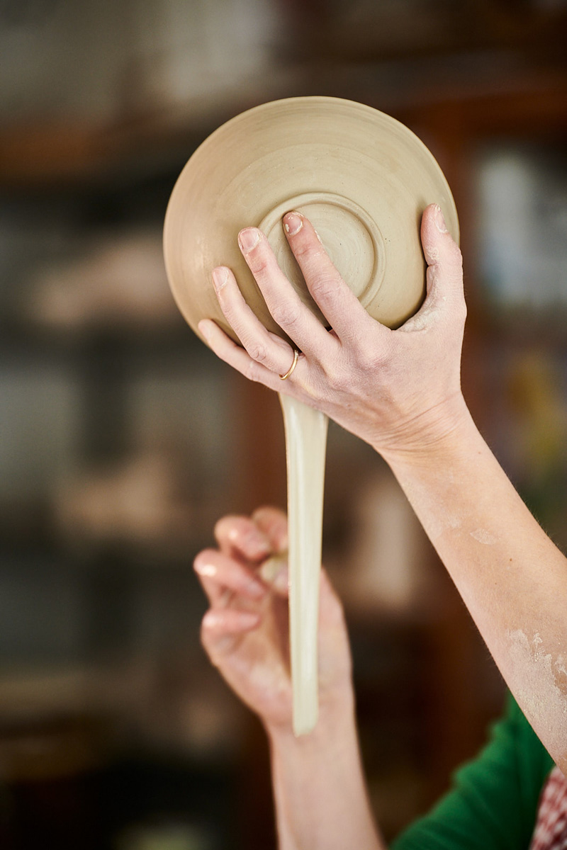 tonschüssel-mit-fluessigem-Ton Tonschüssel wird von einer Hand gehalten. Es wird flüssiger Ton da rausgelassen.
