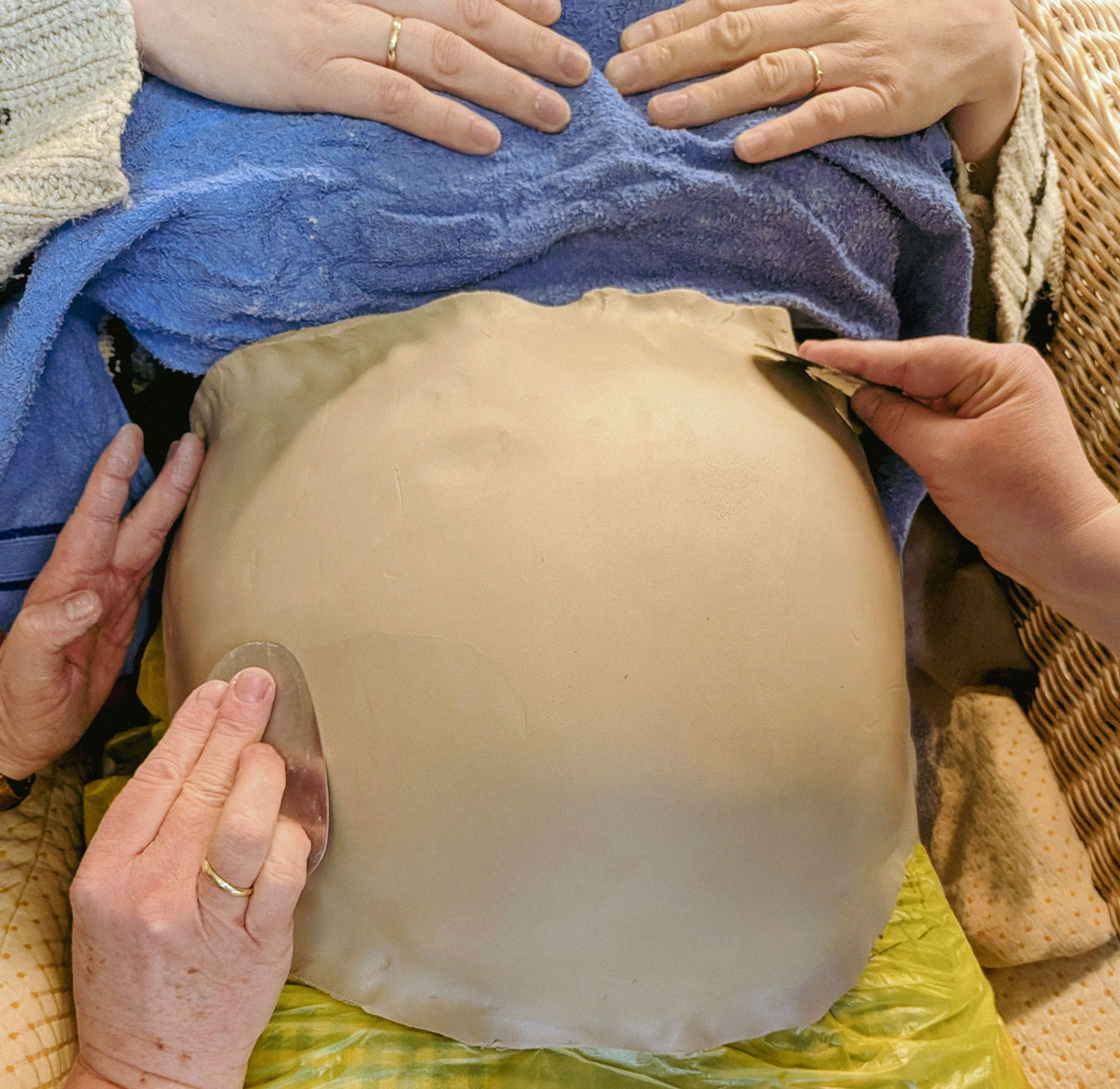 Abdruck einer Billy Bowl. Schwangerschaftsbauch wird mit Ton abgedrückt und zu einer Schale geformt. Auf dem Bild sieht man den Prozess: den Bauch umhüllt von Ton und mehrere Hände, die diesen formen.